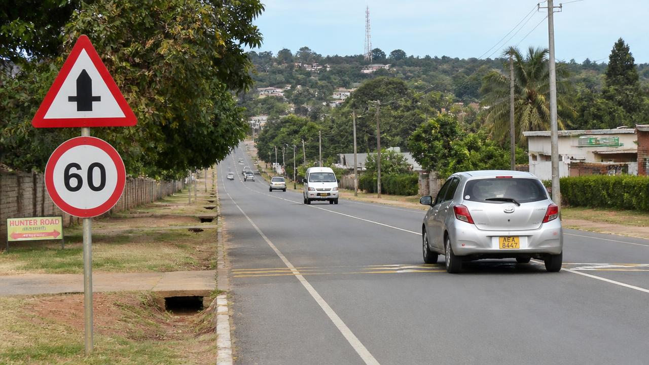 Roadside triangular crossroads warning sign above a circular 60 km/h speed limit sign on a Zimbabwean suburban road.